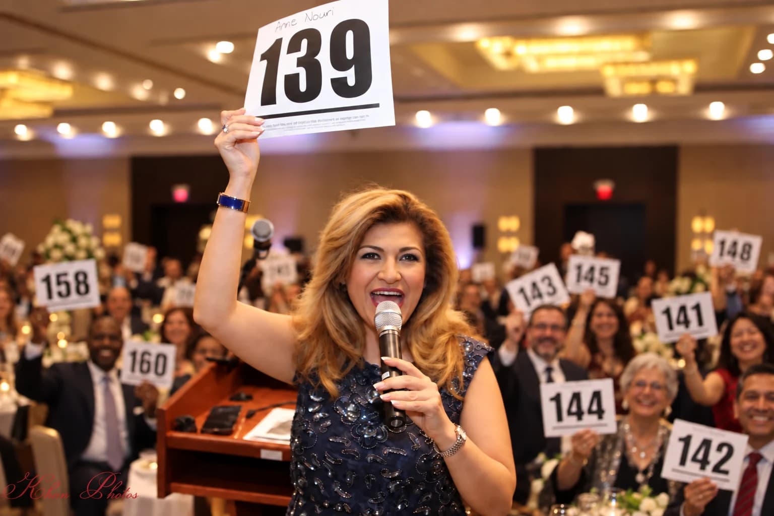 Anne Nouri holding bidder paddle 139 as audience members raise their paddles